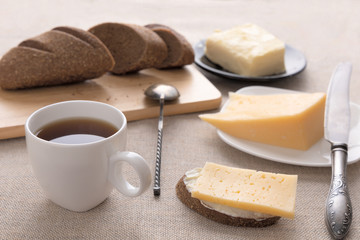 Sliced bread and knife on a cutting board. Butter, cheese, a cup of coffee on a sackcloth. Side view breakfast brunch on table concept
