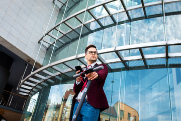 Portrait of businessman with electric scooter standing in front of modern business building.