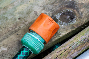Orange garden hose connector set against an old wooden plank with a braided green hose connected to it.