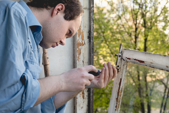 Man repairing old wooden windows using a screwdriver. Repairing interior of old house. Close-up of home DIY
