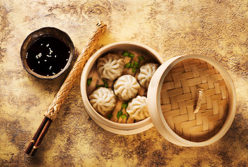 Chinese steamed dumplings in bamboo steamer with soy sauce and chopsticks, top view