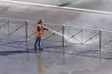 Worker cleaning driveway with gasoline high pressure washer splashing the dirt, asphalt road fence. High pressure cleaning.