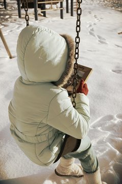 Full Length Of Child Holding Picture Frame While Sitting On Swing During Winter
