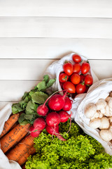 zero waste shopping, organic, bio vegetables concept. Fresh vegetables radish mushrooms carrot salad tomatoes in eco cotton bags on white wooden background. Top view