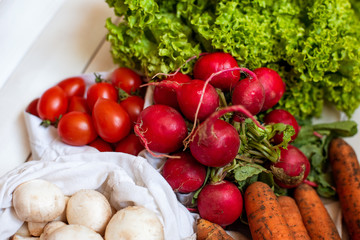 zero waste shopping, organic, bio vegetables concept. Fresh vegetables radish mushrooms carrot salad tomatoes in eco cotton bags on white wooden background. Top view
