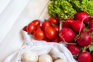 zero waste shopping, organic, bio vegetables concept. Close up photo of fresh vegetables radish mushrooms carrot salad tomatoes in eco cotton bags on white wooden background. Top view