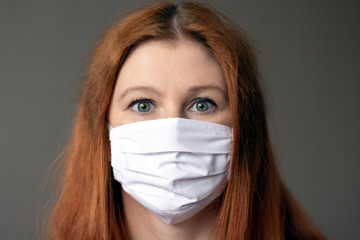 Portraite of a young red-haired woman wearing respiratory medical mask looking to the camera. Coronavirus 2019-ncov covid-19 concept.