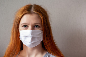 Portraite of a red-haired young woman wearing respiratory medical mask. Coronavirus 2019-ncov covid-19 concept. Space for text.