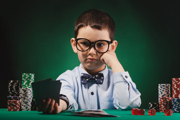 Little kid playing poker in a casino. Studio concept on blue background