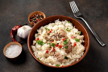 Homemade pilaf with meat and spices in a bowl on a stone table. Eastern cuisine.