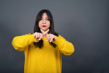 Young beautiful brunette girl wearing casual clothes over isolated background standing against gray wall. Has rejection angry expression crossing fingers doing negative sign.