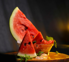 Fresh cocktail of watermelon juice glass and served with piece of watermelon and mint leaves over black slate background and wooden table. Healthy eating and drinking concept.