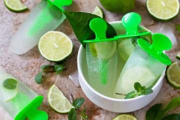 Homemade popsicles with lime juice and mint, mojito fruit ice on a light stone or slate background.