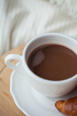 A cup of hot cocoa, a croissant, a wooden stand on the bed. Quarantine time. Homeliness.