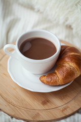 A cup of hot cocoa, a croissant, a wooden stand on the bed. Quarantine time. Homeliness.