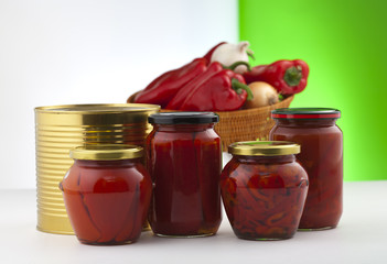 Canned peeled peppers in glass jars. In the background, fresh vegetables are defocused.