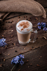 A glass with latte macchiato on wooden background with blue flowers