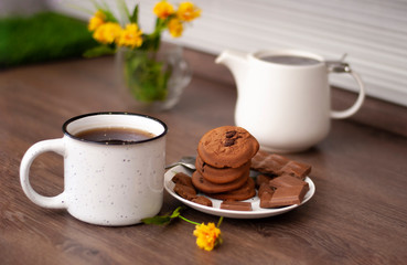 Kitchen table with white kettle and tea cup and cookies chocolate pieces. Close-up view of tasty home Selective focus