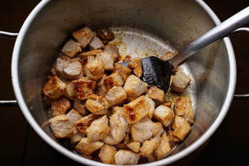 Pieces of pork meat are seared in a stainless steel pot to get roasted aroma for a hearty stew,...
