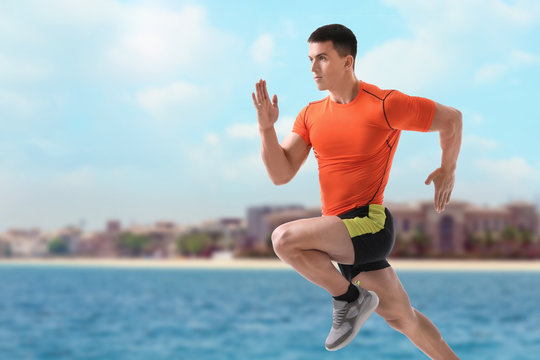 Athletic young man running near sea on sunny day, space for text