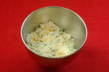 Dry biscuit ingredients with shredded cheese and chopped jalapeno peppers in stainless steel mixing bowl on red tablecloth