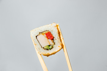 One sushi roll held by chopsticks on a white background - 344613703