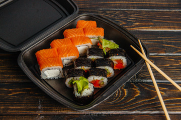 The concept of non-contact delivery of sushi rolls. Black packaging with different rolls and craft package on a wooden table. - 344614305
