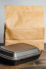 A brown craft paper bag and a black container for taking out or delivering goods and food on a wooden table. Place for advertising. delivery service concept - 344614581