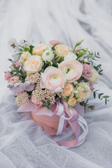 A large flower arrangement in a pink hat box was created by a florist for a wedding gift. White Freesia , pink Ranunculus asiaticus, eustoma flowers, roses and eucalyptus in a bouquet.