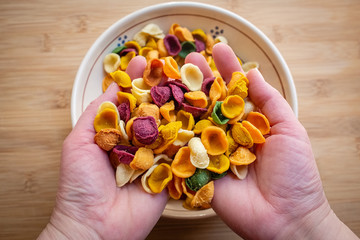 Female hands holding coloured orecchiette, fresh pasta made with vegetables and spices. Apulia typical food. Italy