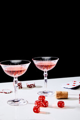 glasses of cocktail, dice, cork, casino chips and pack of cards on white surface isolated on black