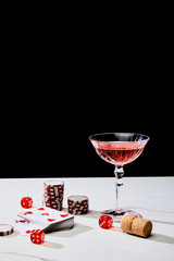 deck of cards, glass of cocktail, dice, casino tokens and cork on white surface isolated on black
