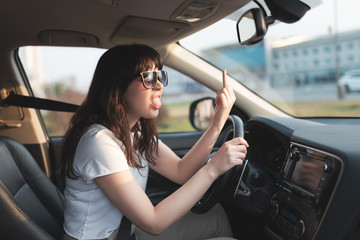Naklejka premium Portrait of aggressive brunette woman showing middle finger to somebody while driving a car.