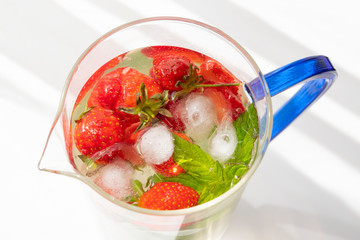 A blue handle glass carafe with high PH level detox water to boost the immune system to fight corona virus. Ingredients are strawberries, ice and mint leaves