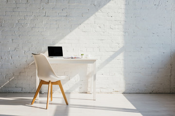 home office with table, chair and laptop with blank screen in sunlight
