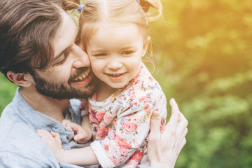 Fototapeta na wymiar stylish bearded father with his little daughter in his arms against the backdrop of green trees on a walk in the park hugging and kissing a baby