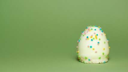 White chocolate Easter egg with multicolored sugar sprinkles isolated on green background, illustration of Easter, Eg, candy, sweetness