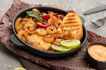 selective focus of fried shrimps with grilled toasts, vegetables and lime on grey concrete background with cutlery