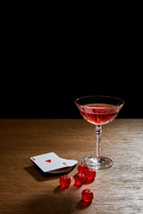 glass of cocktail near deck of cards and dice on wooden surface isolated on black
