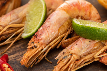 close up view of fried shrimps with chili and lime on wooden board