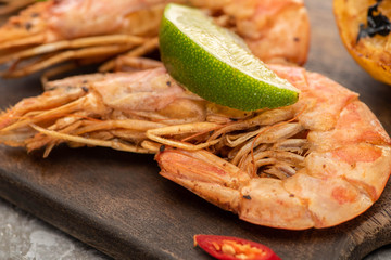 close up view of fried shrimps with chili and lime on wooden board