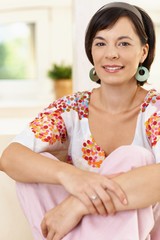 Portrait of happy young woman looking at camera sitting on sofa at home.