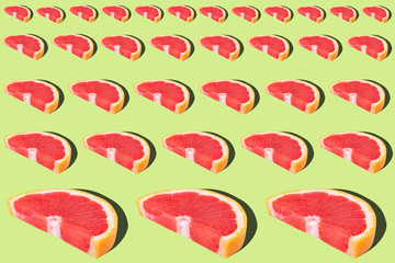 Flat lay fruit pattern of fresh grapefruit slices on green background.