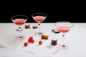glasses of cocktail, dice, cork, casino chips and playing cards on white surface isolated on black