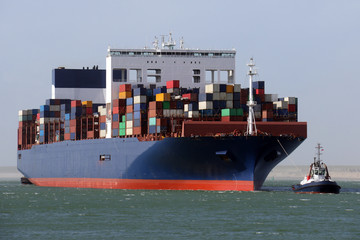 blaues Containerschigg mit Hafenschlepper