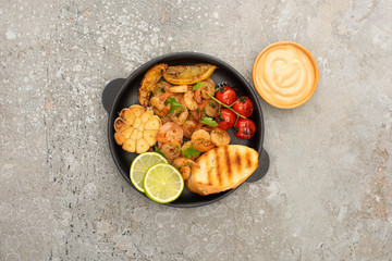 top view of fried shrimps with grilled toasts, vegetables and lime near sauce on grey concrete background