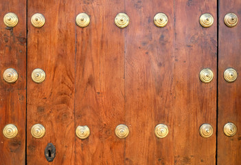 Classic vintage varnished wooden door with golden metal buttons and a keyhole.