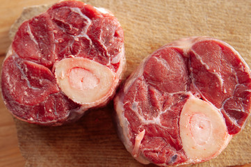 Two pieces or slices of big bone with few drops of blood and meat on side. Bones are placed on desk.