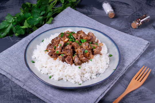 Stewed chicken gizzards on the boiled rice. Hot meal with offal meat products