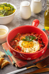 shakshuka in a red pan, coffee, bread  and salad in a bowl, gray background, copy space
